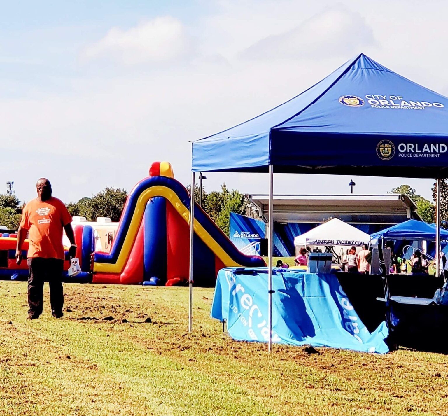 An event on a grassy field with inflatable slides and tents; a man in orange shirt walks by.