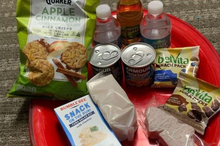 A red tray holding snacks and drinks including rice cakes, drinks, canned meat, and breakfast biscuits.