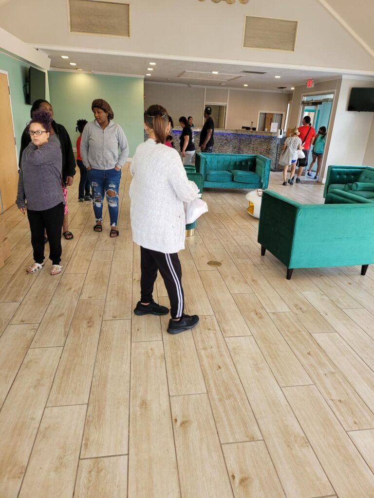 People gathered in a room with teal furniture, holding papers, and looking towards an open doorway.
