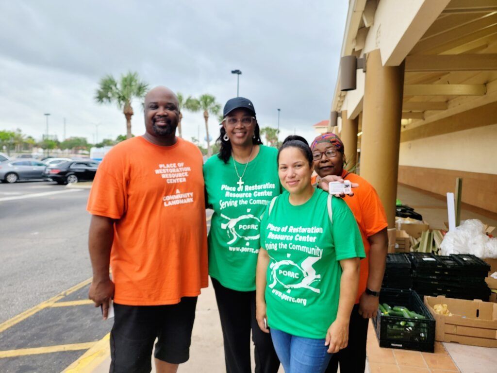 Four people in front of a building; two in orange shirts, two in green shirts with a logo.