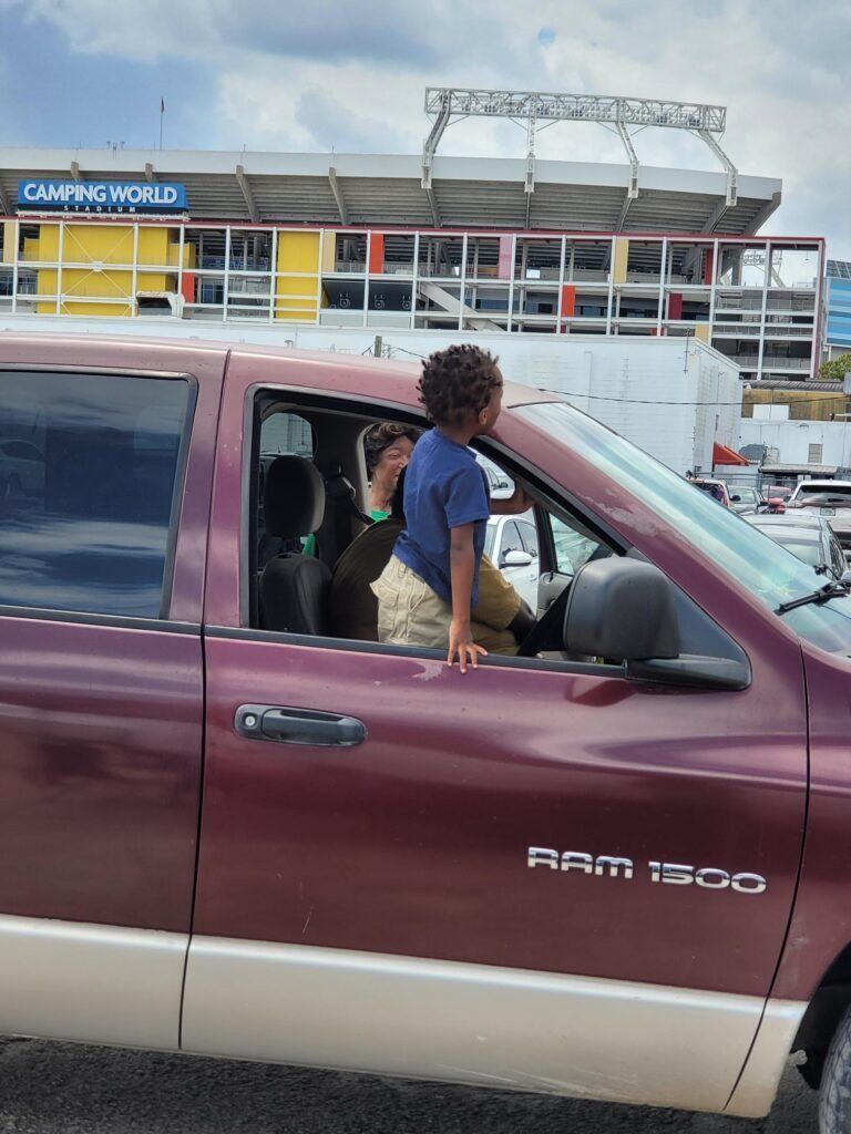 A child leans out of a maroon Ram 1500 truck window, with a stadium in the background.
