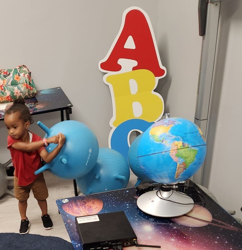 Child playing with a blue exercise ball and globe in a playroom with large ABC letters.