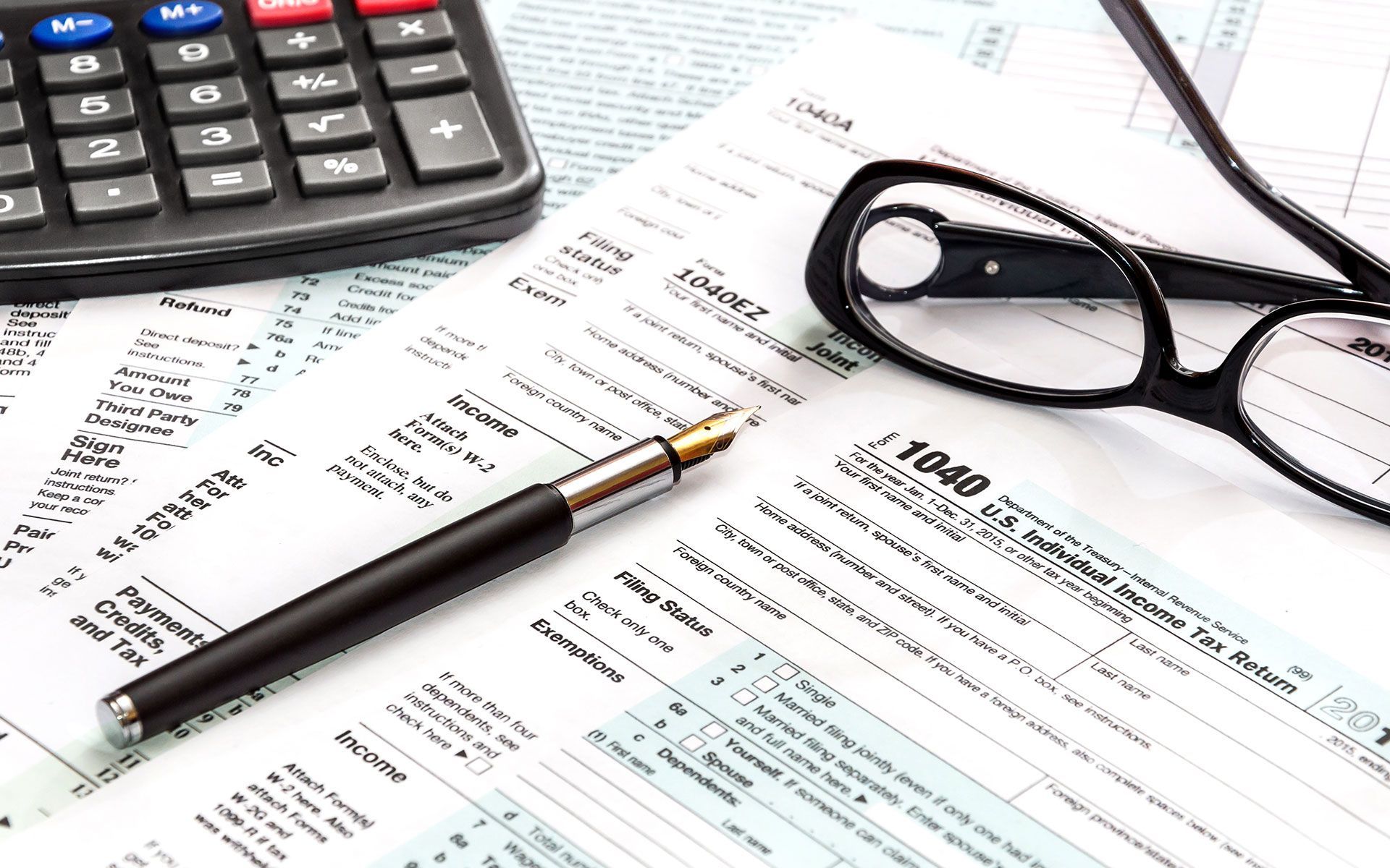 Calculator, glasses, pen, and tax forms on a desk, for tax preparation.