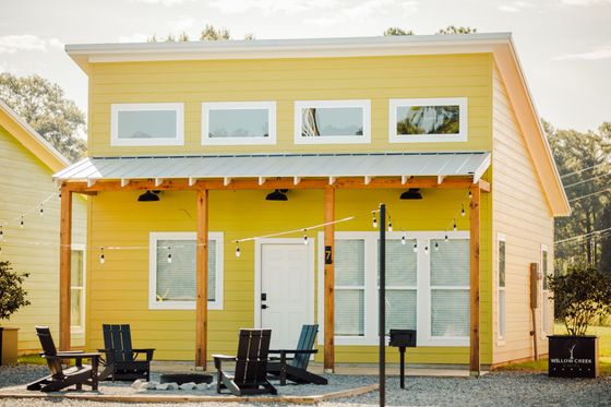 A yellow house with a porch and chairs in front of it.