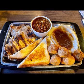 Three sliders on a plate next to a glass of beer on a wooden table.