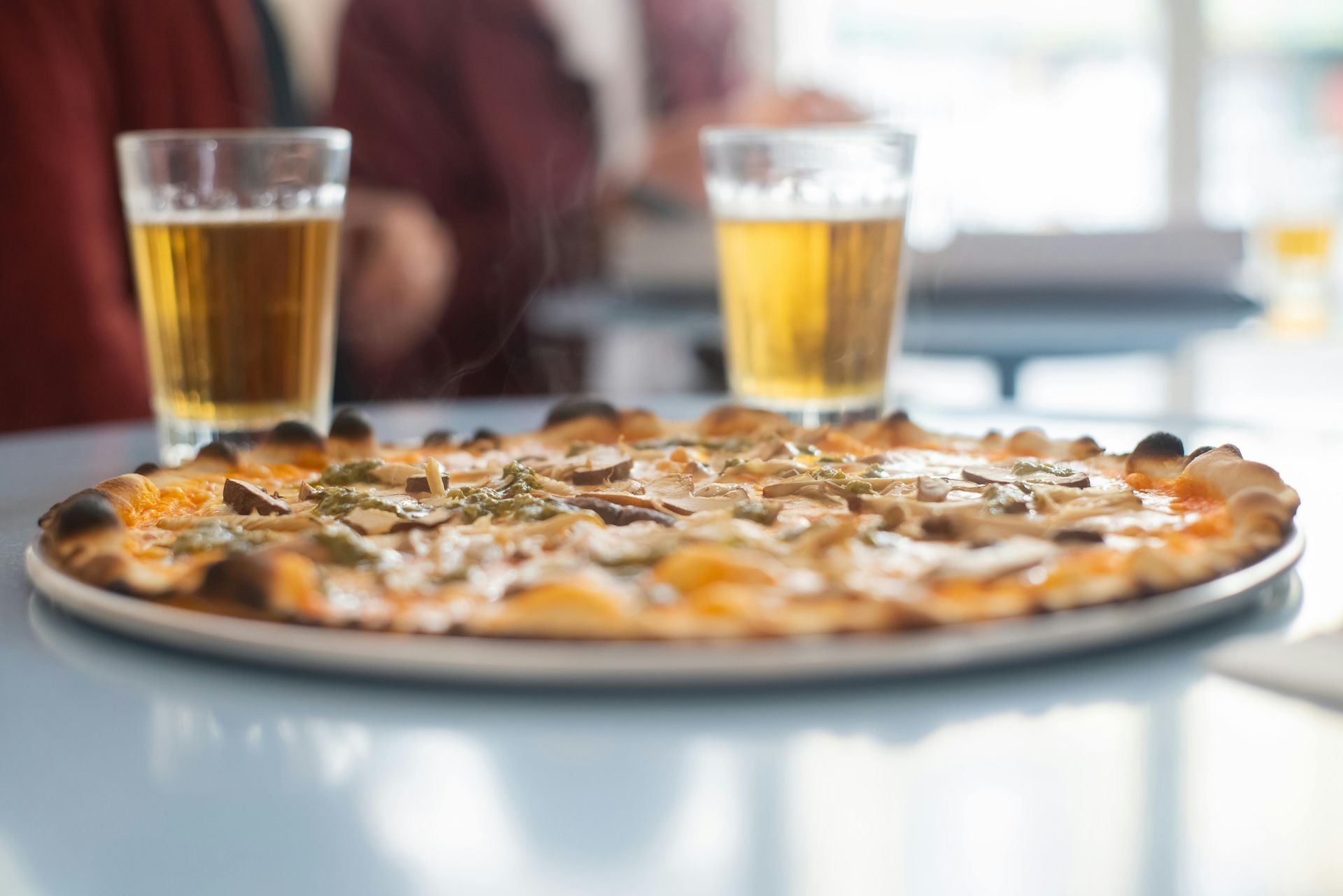 A pizza and two glasses of beer on a table.