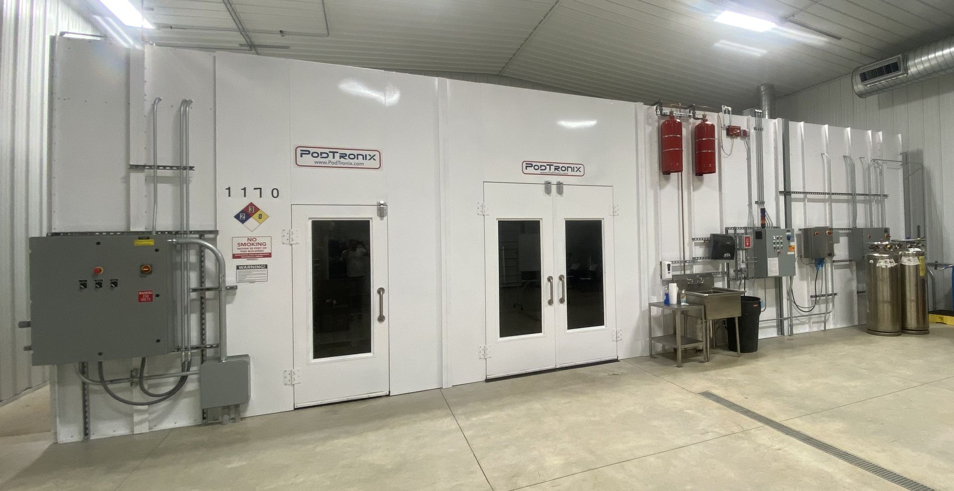 Large white paint booth inside a building, with doors and equipment.