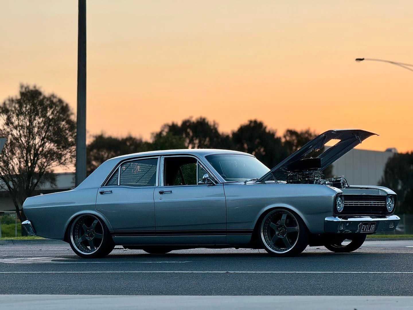 A silver car with the hood up is parked on the side of the road.