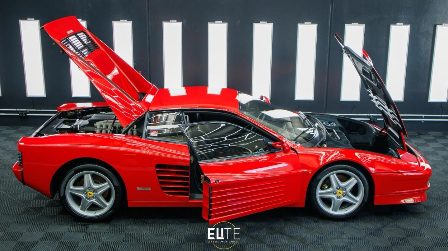 Red Ferrari Testarossa with doors and engine compartments open, in a showroom with black and white stripes.