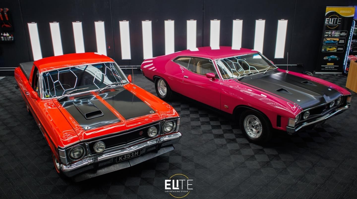 Two vintage Ford cars: red pickup and pink coupe with black hoods, on a black and white tiled floor.