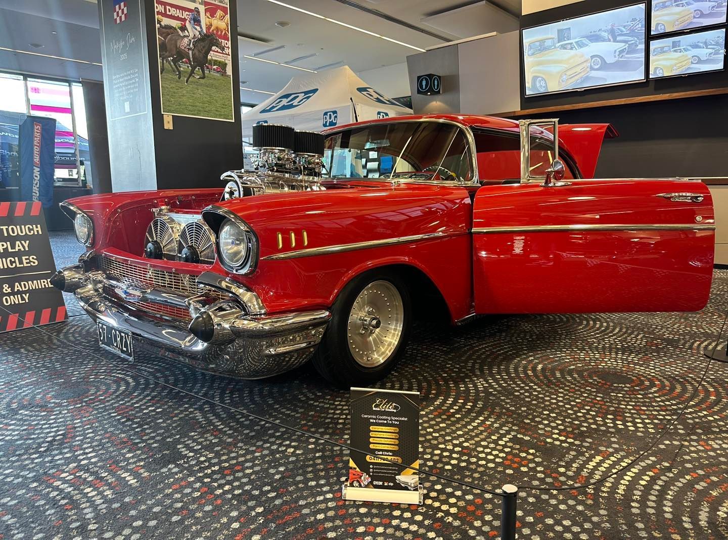 A red car with the hood up is on display in a room.