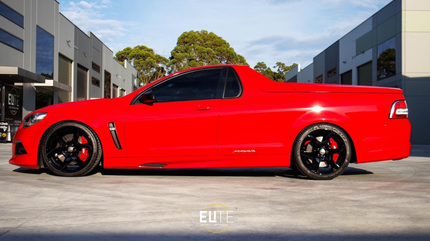 Red Holden ute with black wheels and tinted windows parked in front of a building.