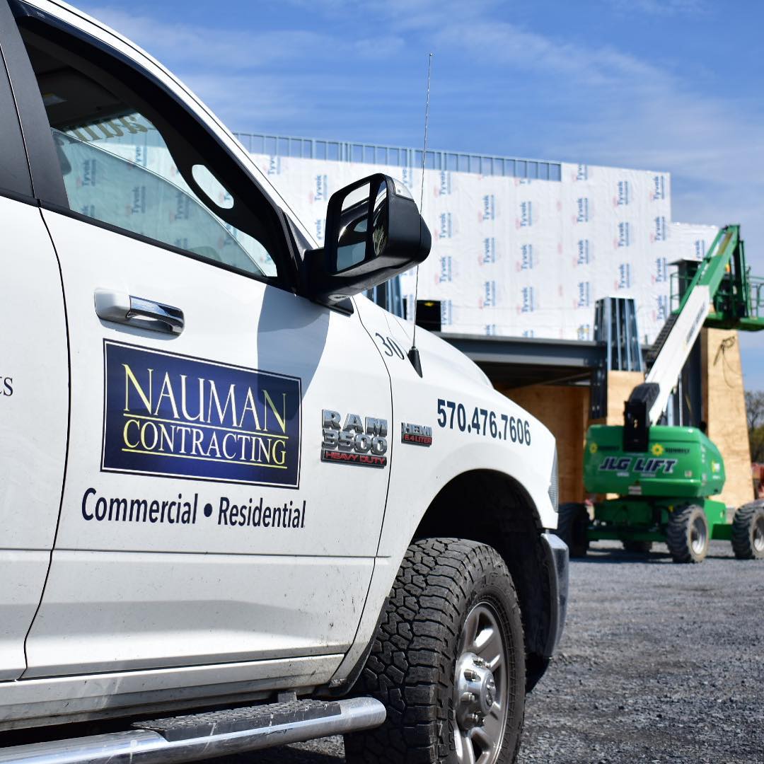 A white nauman contracting truck is parked in front of a building under construction.