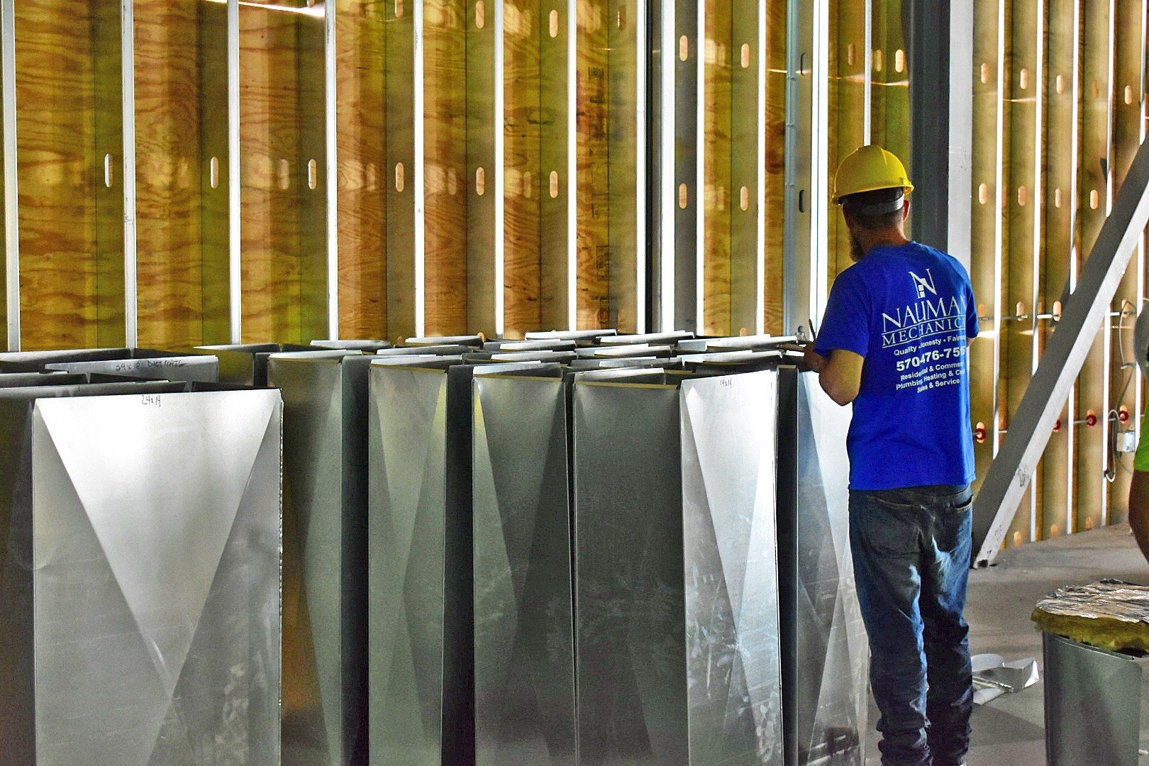 A man from Nauman Inc. wearing a hard hat is standing in front of a row of metal pipes.