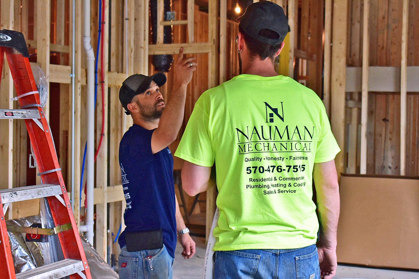 Two Nauman construction workers are standing in a room with a ladder.