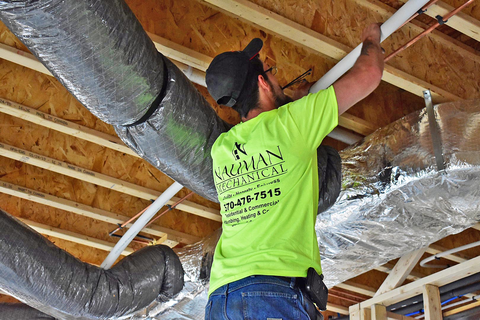 A man from Nauman Inc. in a neon yellow shirt is working on a ceiling.