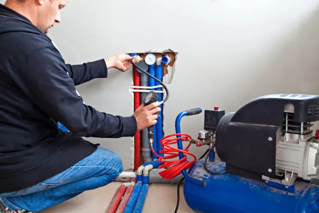 A man is kneeling on the floor working a heating system. 