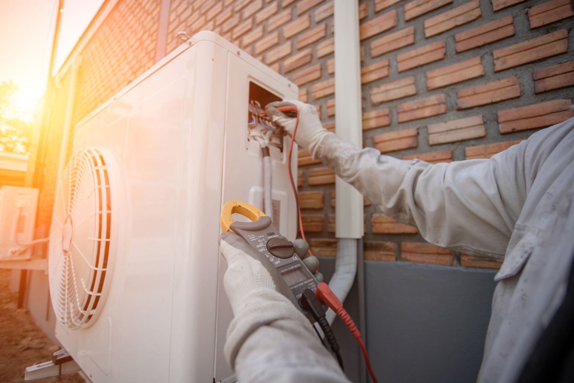 HVAC technician using a multimeter to check an AC unit outside a brick building. HVAC technician using a multimeter to check an AC unit outside a brick building.