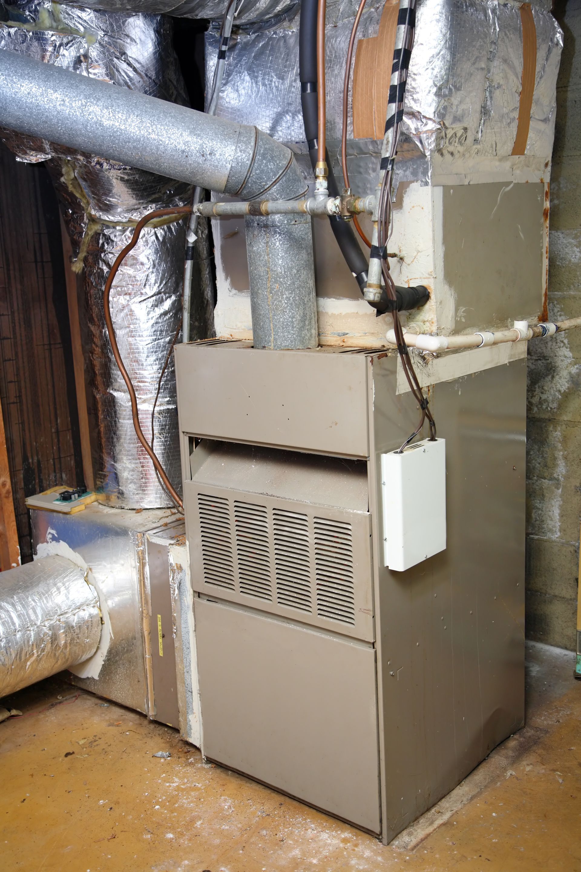 A metal HVAC furnace with ductwork in a basement setting.