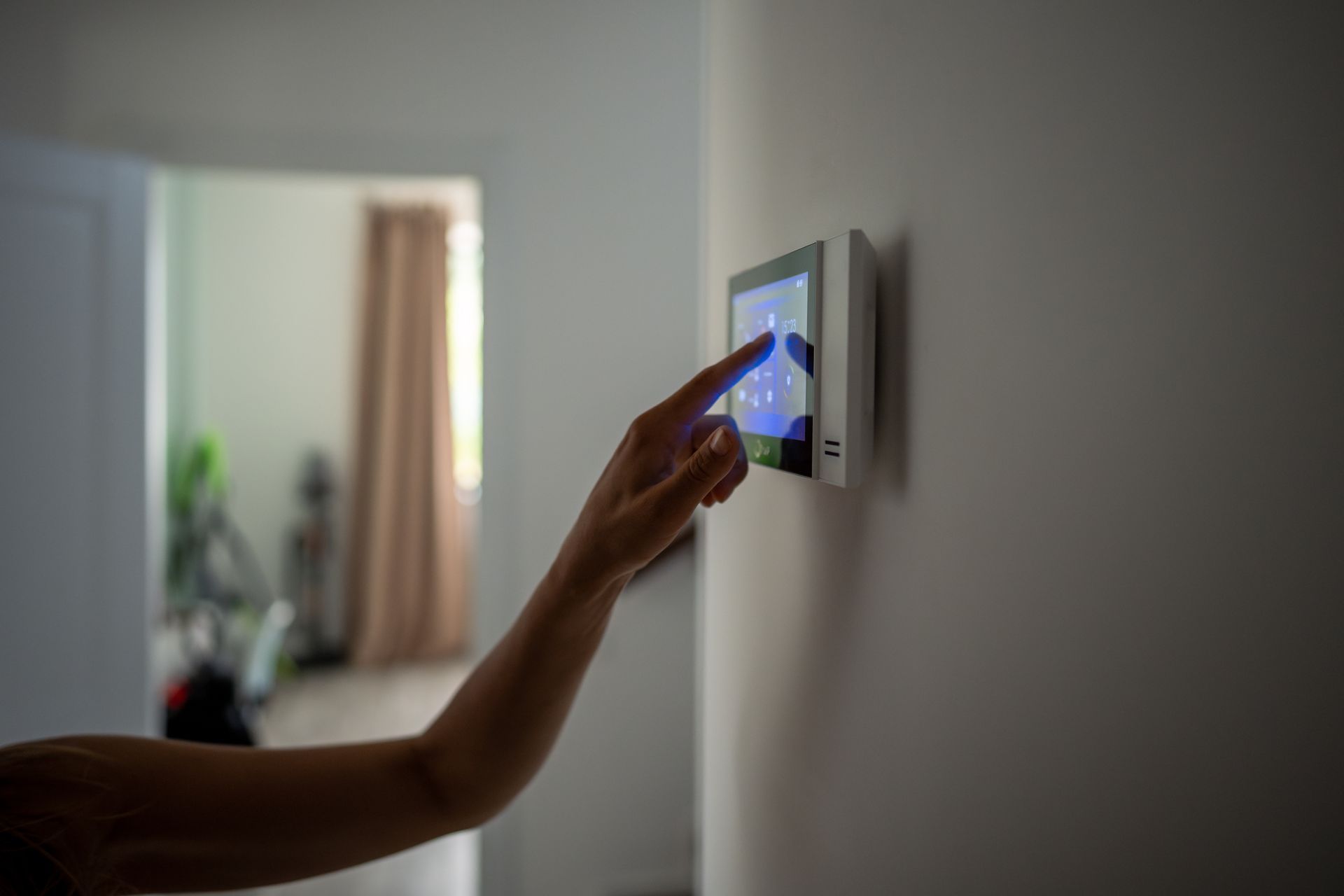 A person's hand touches a touchscreen control panel on a white wall inside a home. A person's hand touches a touchscreen control panel on a white wall inside a home.