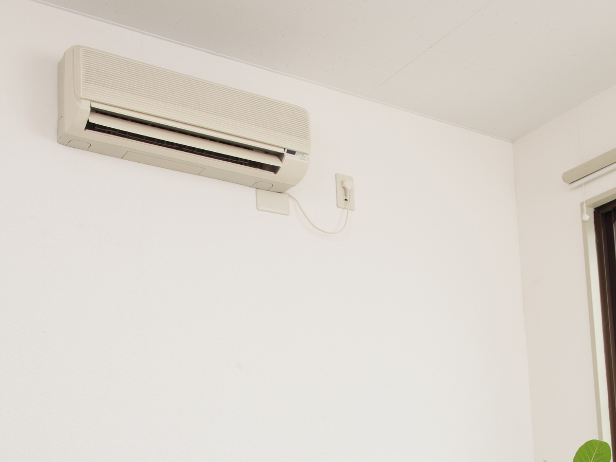 A white air conditioner is mounted on a white wall next to a window.