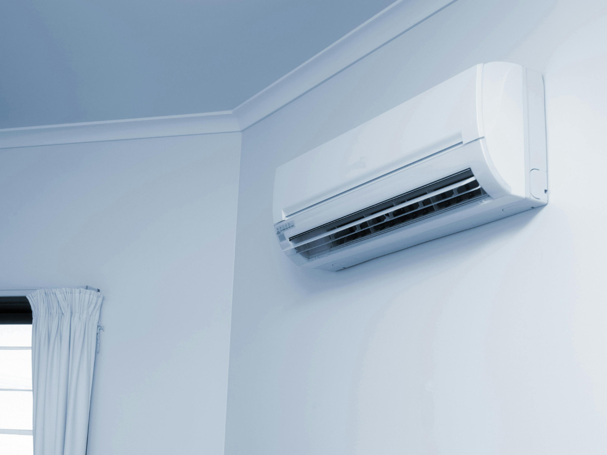 A white air conditioner is mounted on a white wall next to a window. A white air conditioner is mounted on a white wall next to a window.