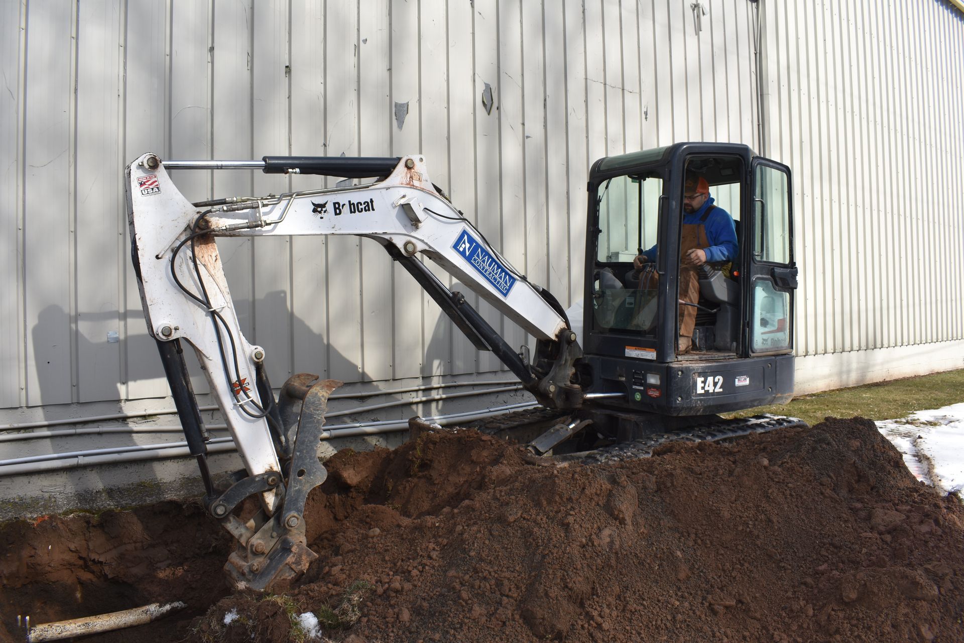 A small Nauman Inc. excavator is digging a hole in the dirt in front of a building.