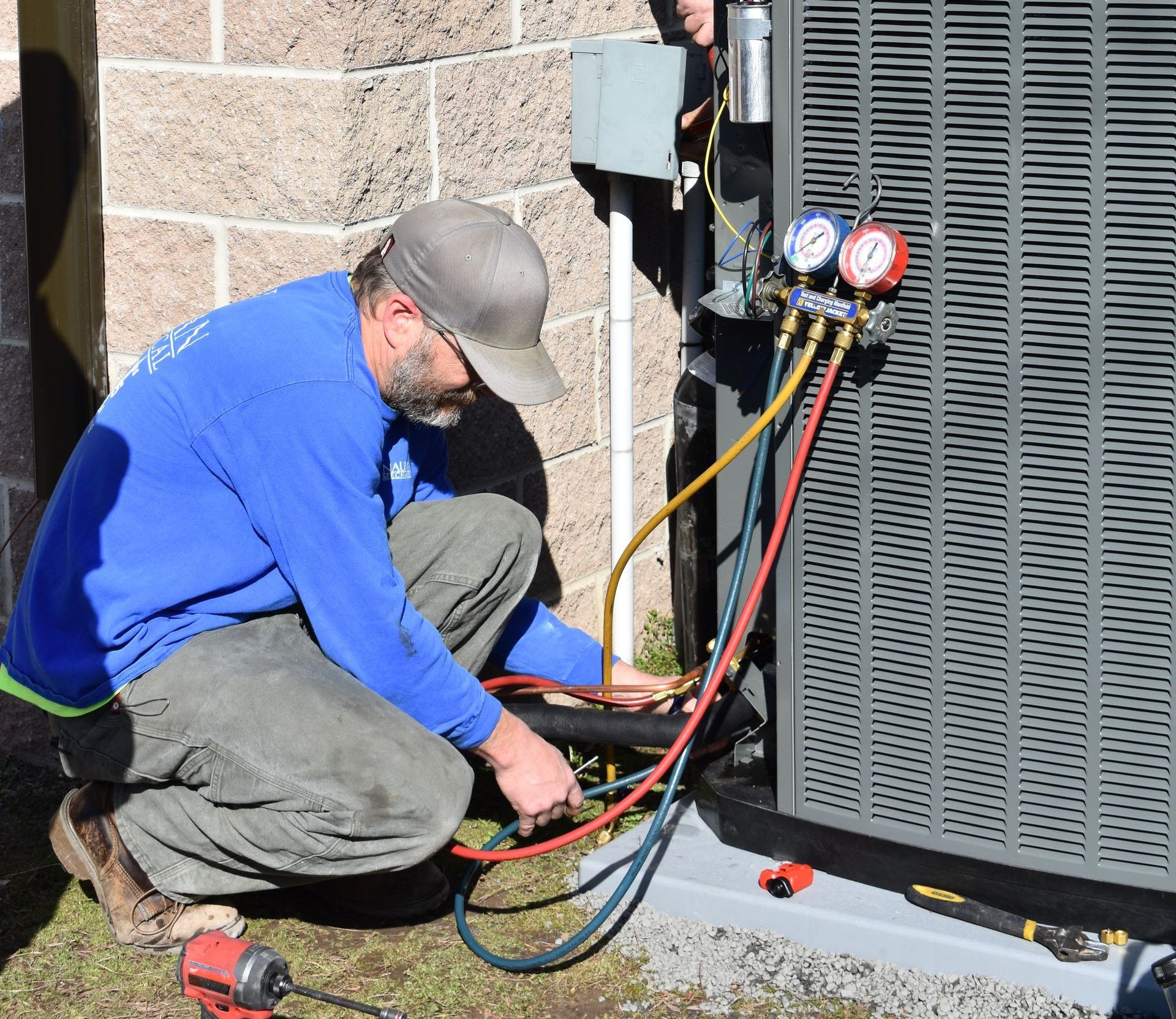 A man in a blue shirt from Nauman Inc. is working on an air conditioner