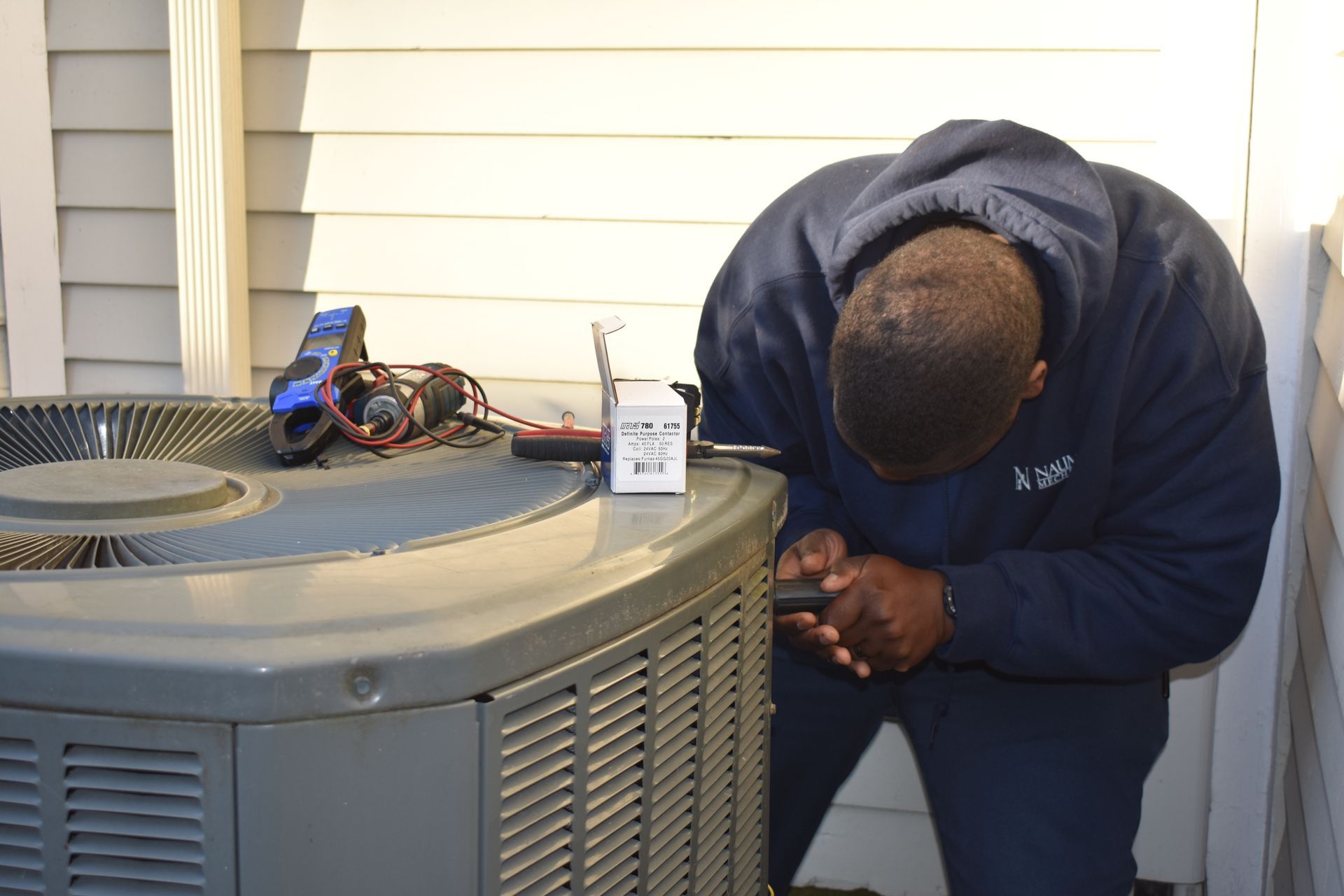 A man from Nauman Inc. is working on an air conditioner outside of a house.