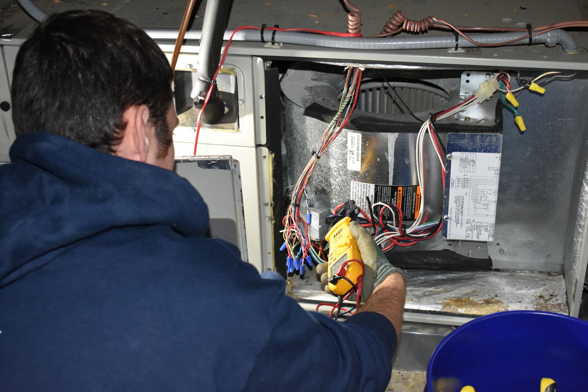 A man from Nauman Inc. is working on an air conditioner with a multimeter.