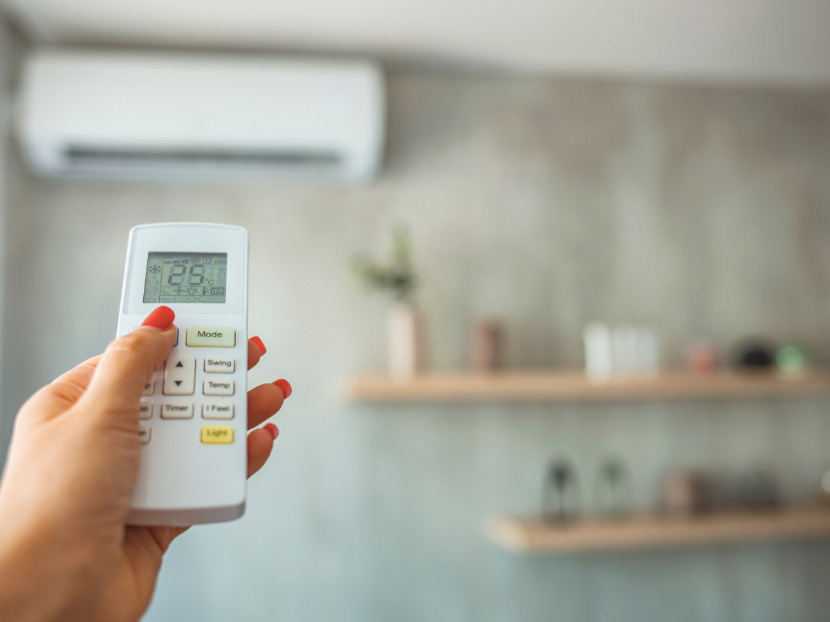 A woman is holding a remote control in front of an air conditioner.