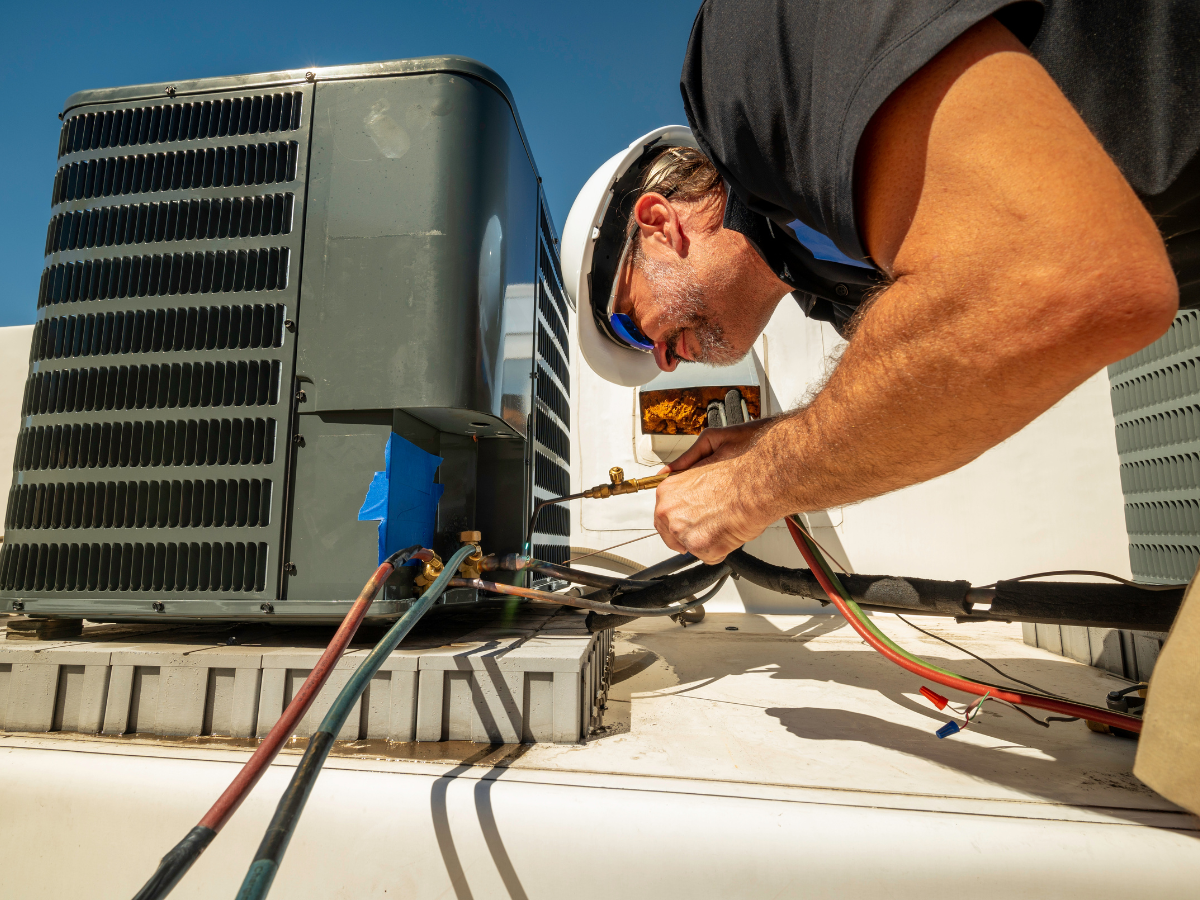 A man is working on an air conditioner on the roof of a building.