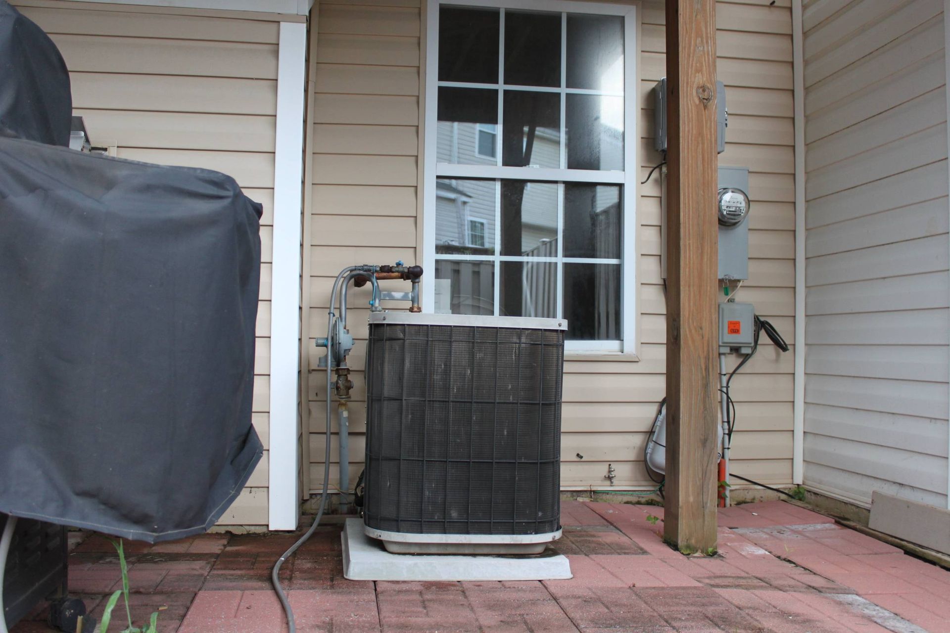 An air conditioner is sitting outside of a house next to a window.