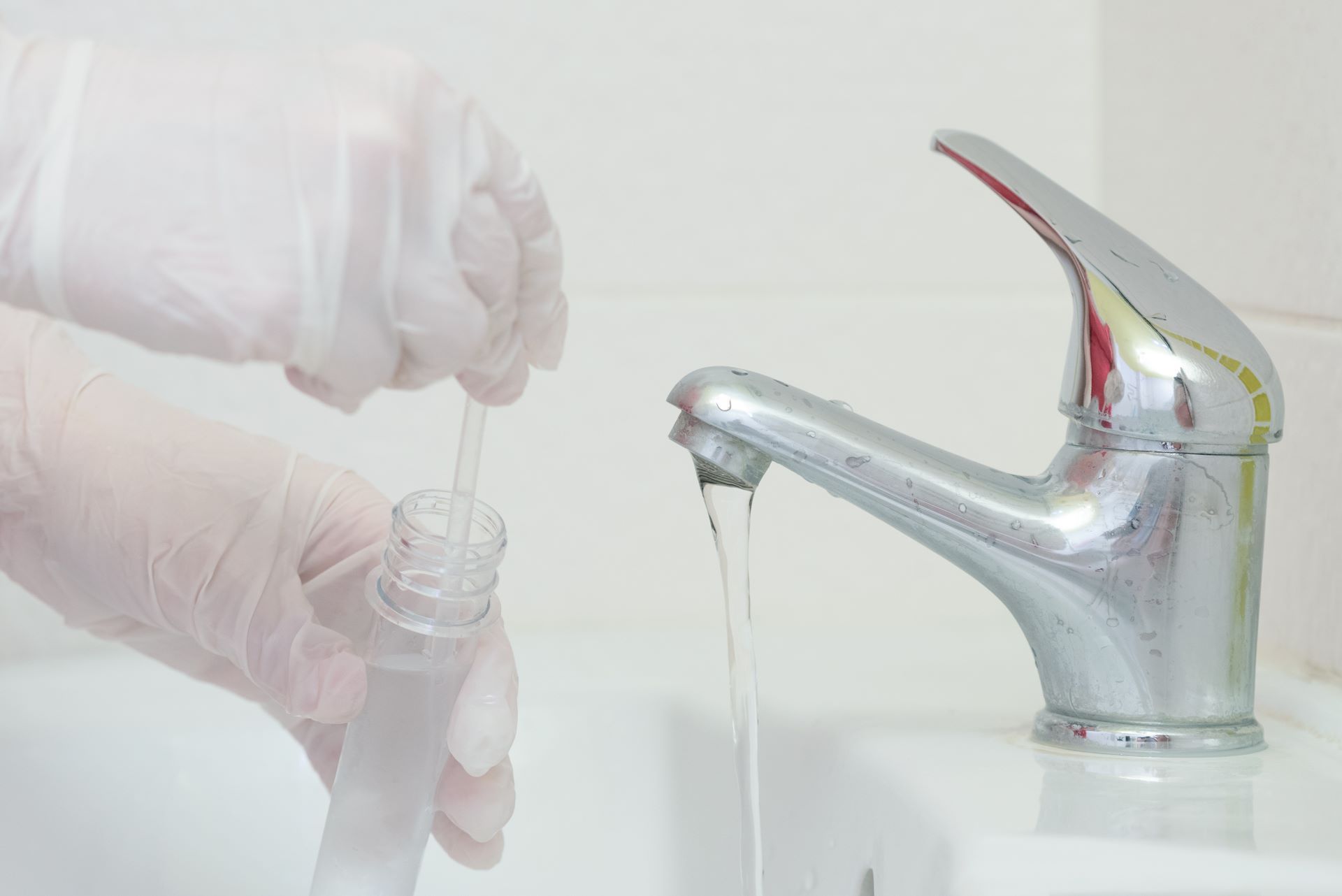 Person with gloved hands taking a sample of water from a sink for quality testing