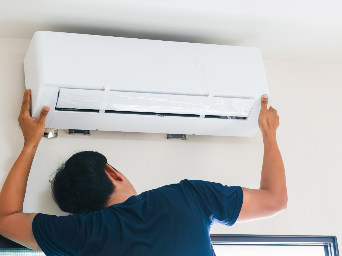 A worker from Nauman Inc. is working on an air conditioner outside of a house.