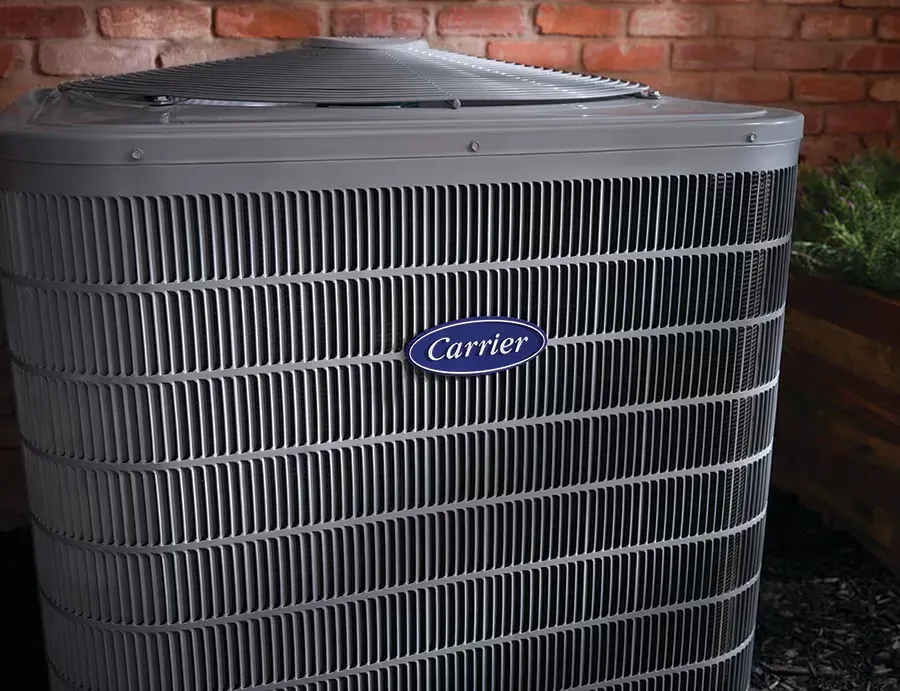 A carrier air conditioner is sitting in front of a brick wall