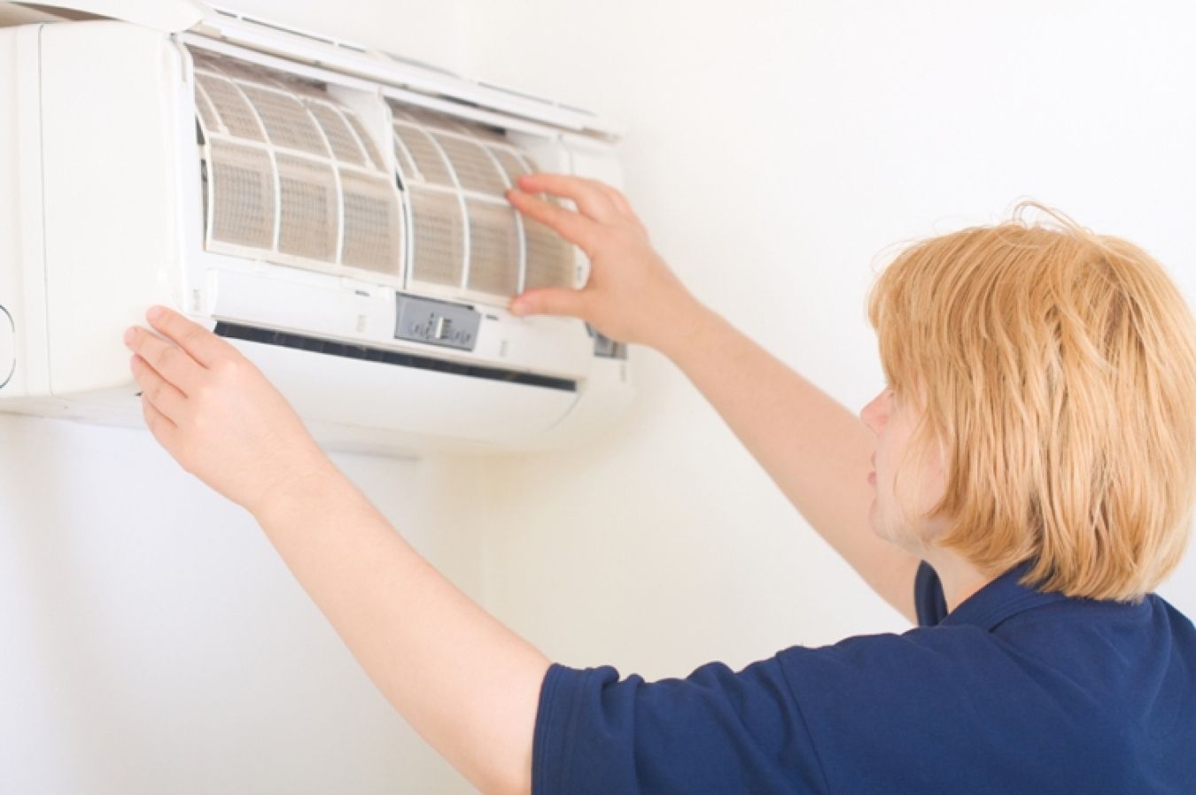 A woman is cleaning the filter of an air conditioner.