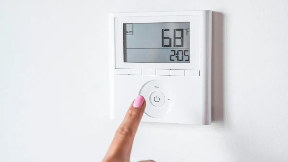 A woman is adjusting the temperature on a thermostat.