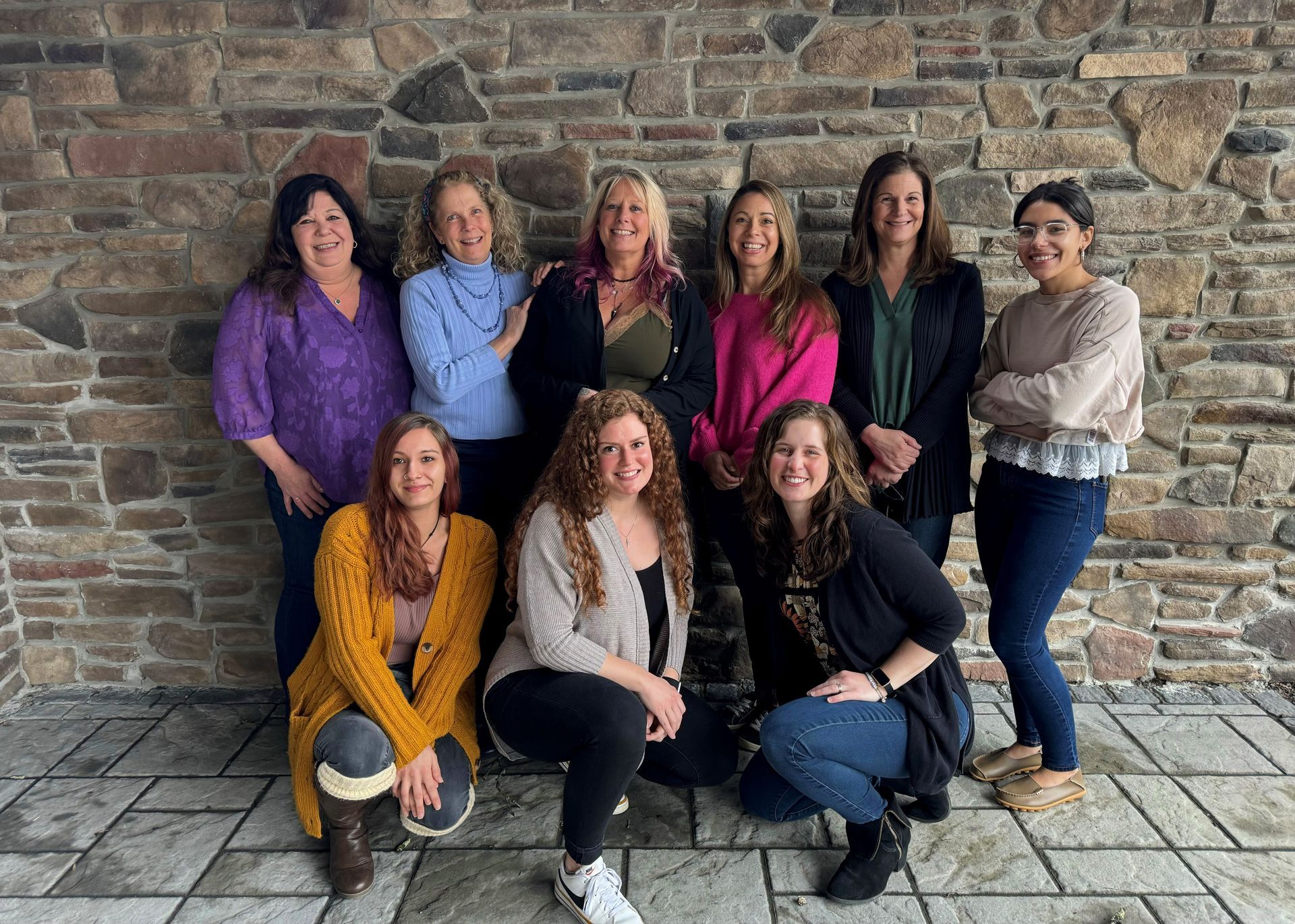 A group of women from Nauman Inc. are posing for a picture in front of a stone wall.