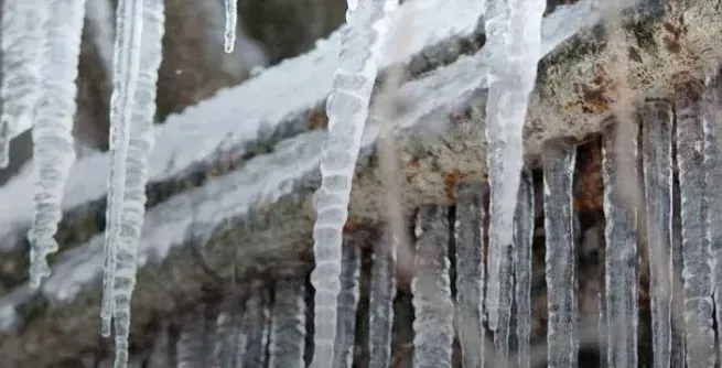 Frozen pipes against a house with icicles hanging down from it. 