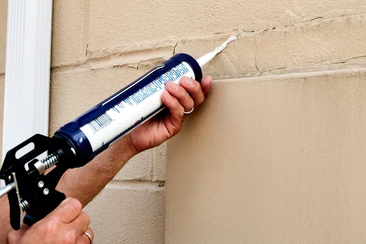 Someone using caulk to reseal cracks on a wall.