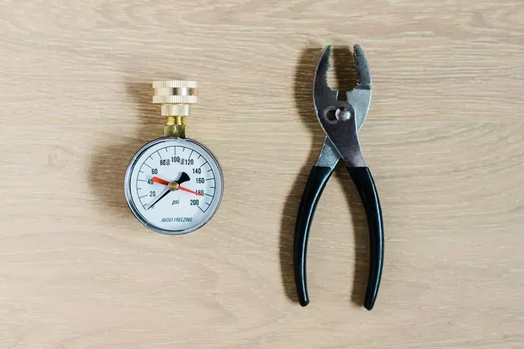 A pressure gauge and pliers are sitting on a wooden table.