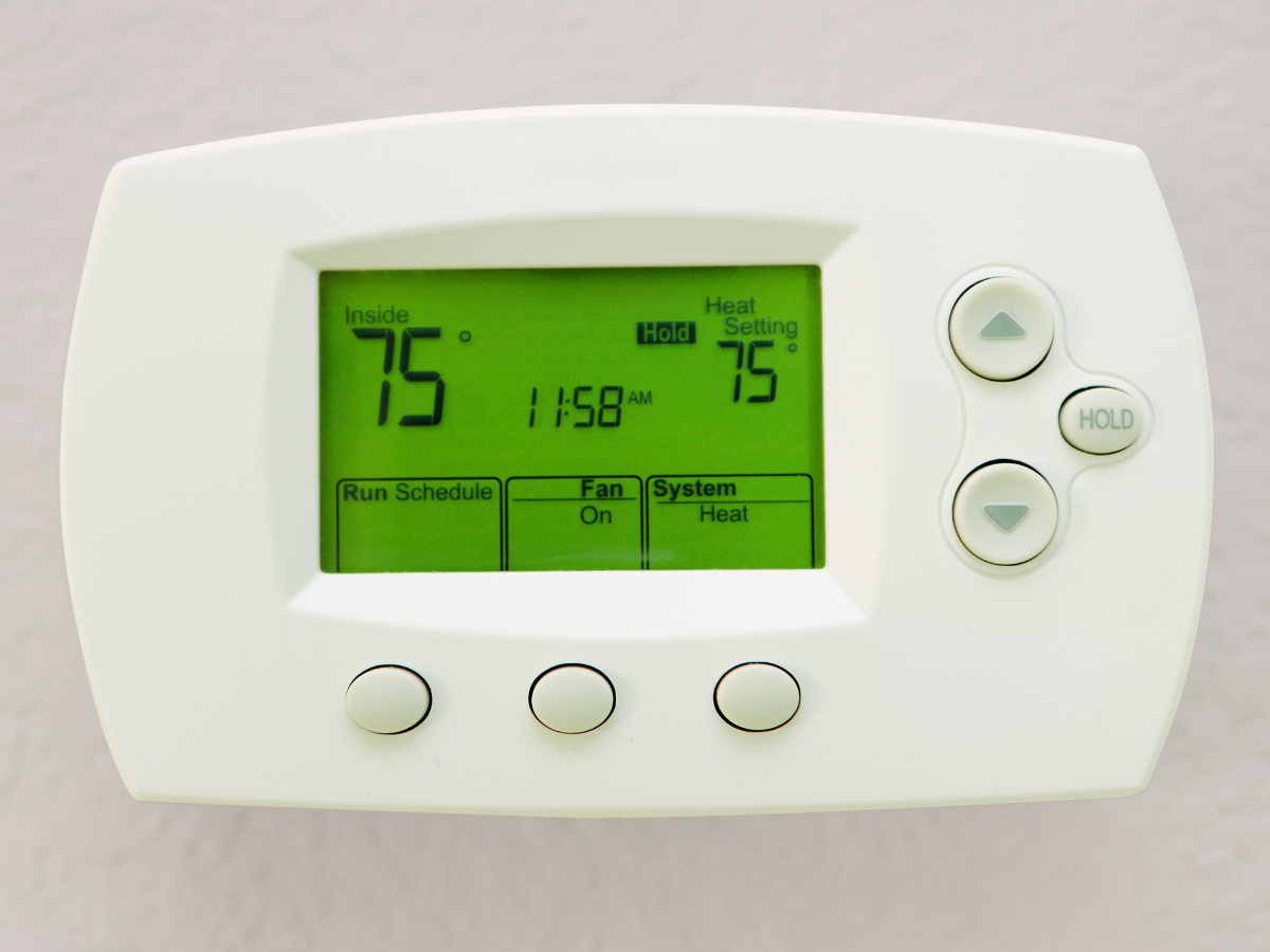 A white thermostat with a green screen displaying 75 degrees
