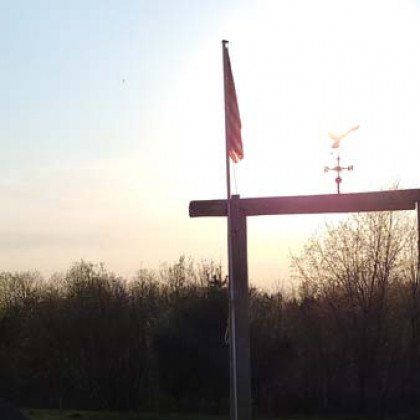 A cross with a flag on top of it and a weather vane.