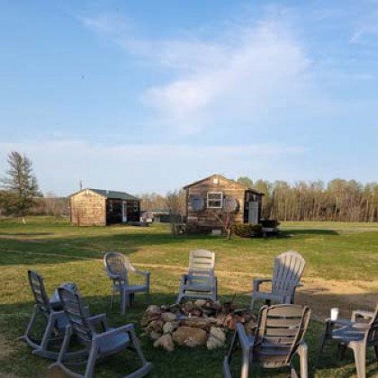 A group of rocking chairs are sitting around a fire pit in a grassy field.