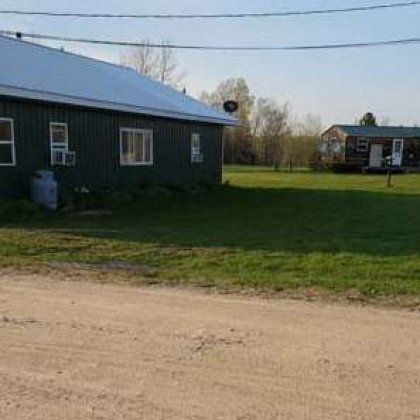 A house is sitting in the middle of a grassy field next to a dirt road.