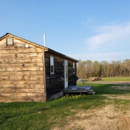 A small wooden house is sitting in the middle of a grassy field.