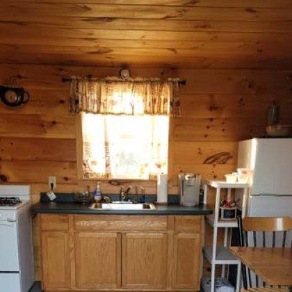 A kitchen in a log cabin with a sink , stove , refrigerator , table and chairs.
