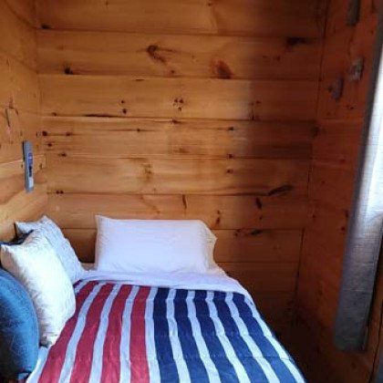 A small bedroom in a log cabin with a bed and a window.