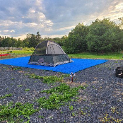 A tent is sitting on top of a blue tarp in a gravel area.